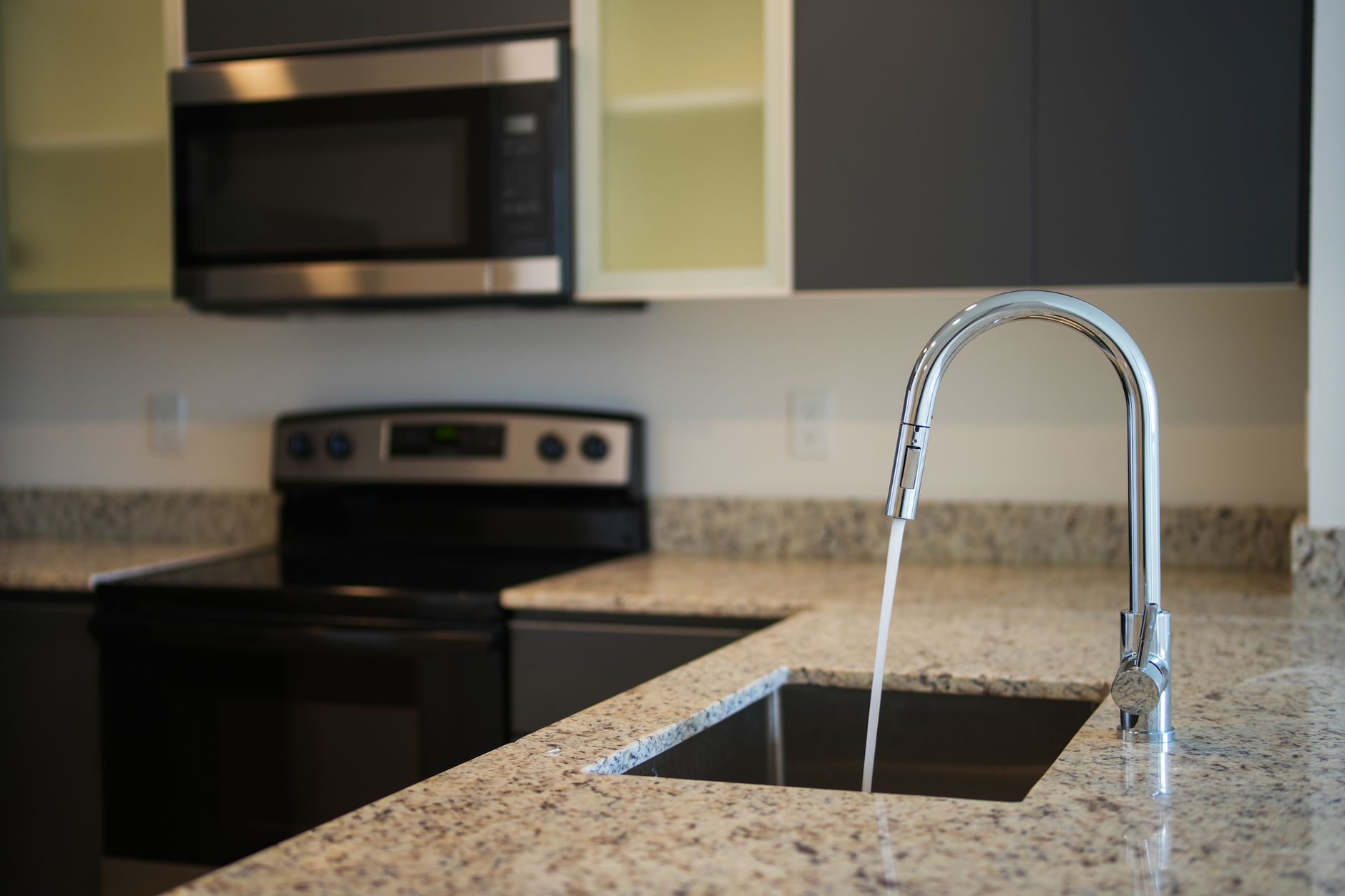 A sleek kitchen faucet on a granite countertop with modern appliances in view in Austin, TX